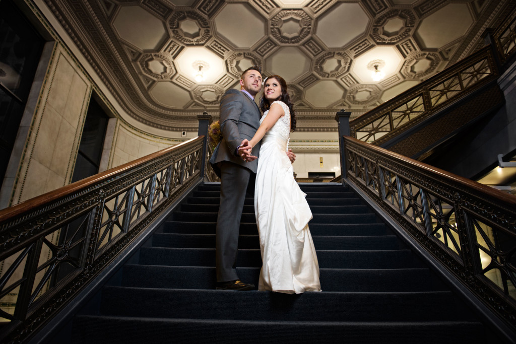 Bride and Groom standing on the vintage staircase holding hands and looking over the camera