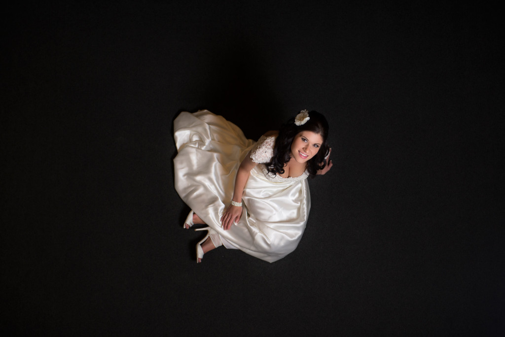 Bride sitting on a dark carpet looking up.