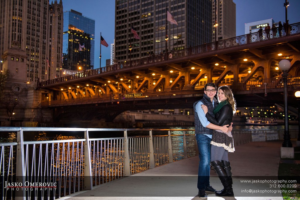 night engagement session at the river walk in Chicago with couple standing together backlighted