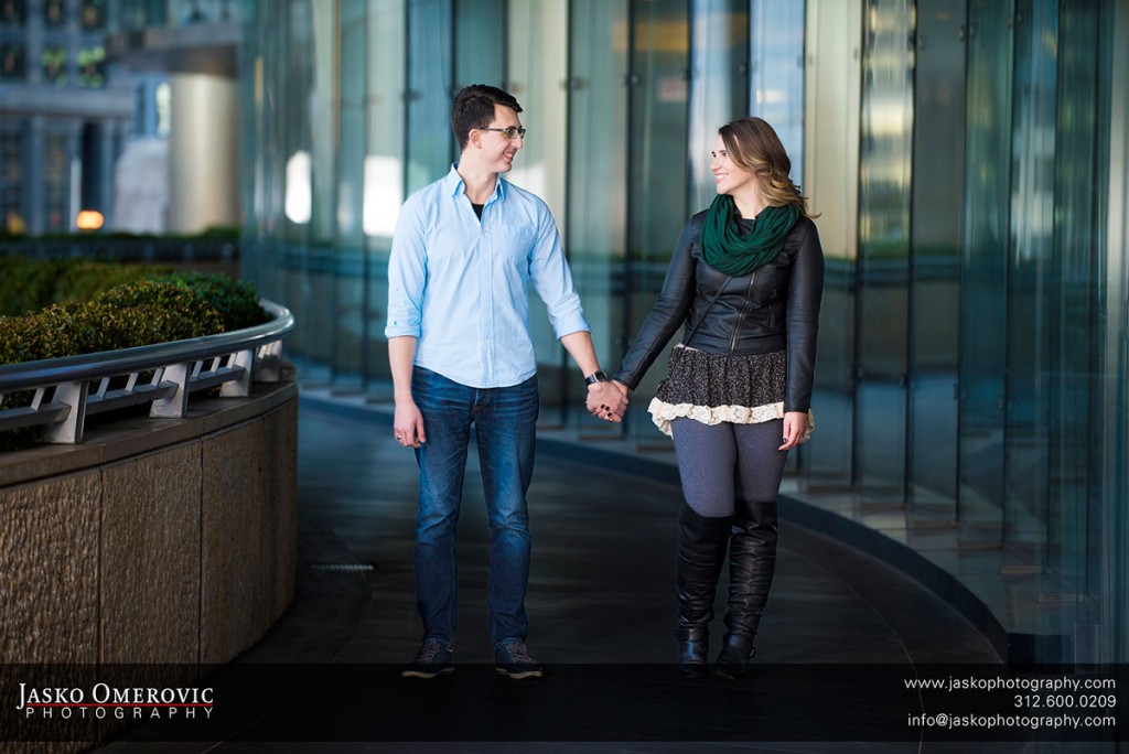 Couple holding hands near trump tower in Chicago surrounded by architectural glass.
