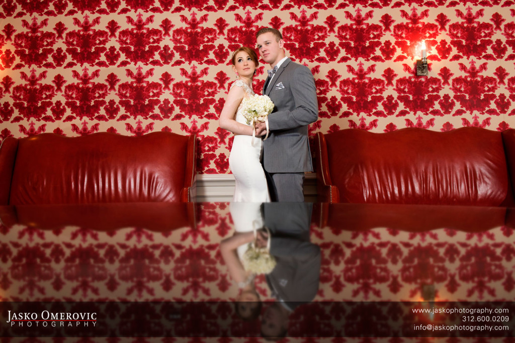 Bride and groom standing together in front of red wallpapaer
