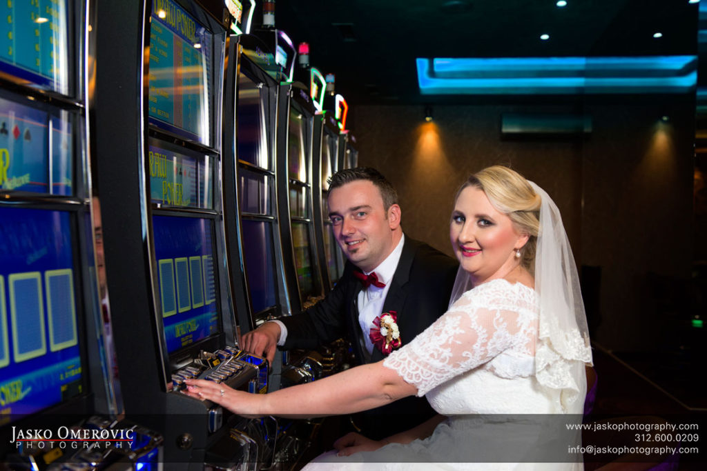Bride and groom sitting at the casino slot machine trying out their luck.