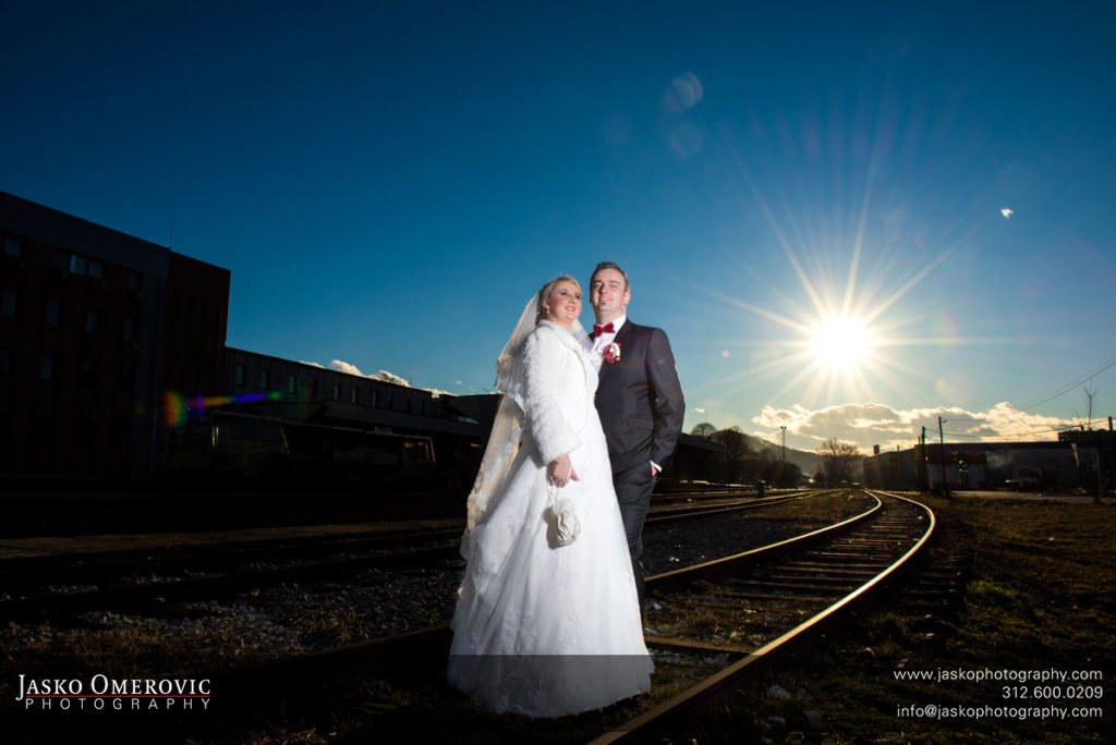 Bride and groom at the tracks of train station with sun in the background