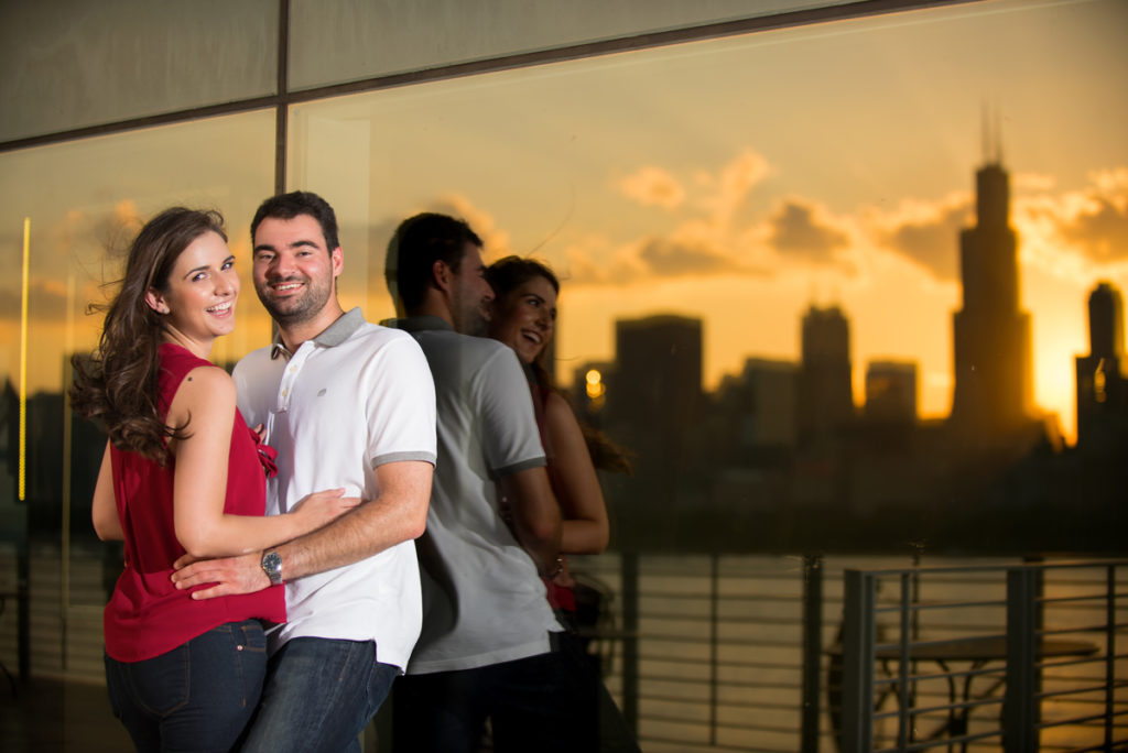 engaged couple leaning agains the glass with amazing city reflections in the back glass