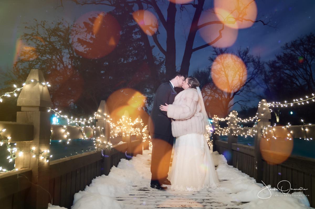 bride and groom kissing in a night photo on the bridge covered in snow