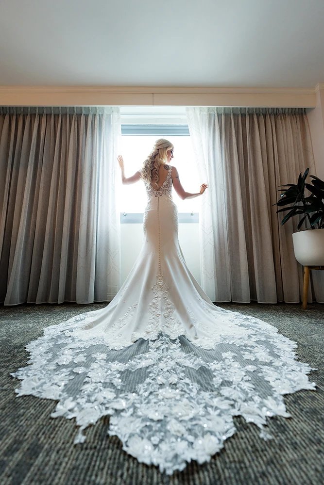 bride portrait with showing wedding dress details and long train against the window, light and airy lighting gently holding the curtains on the window