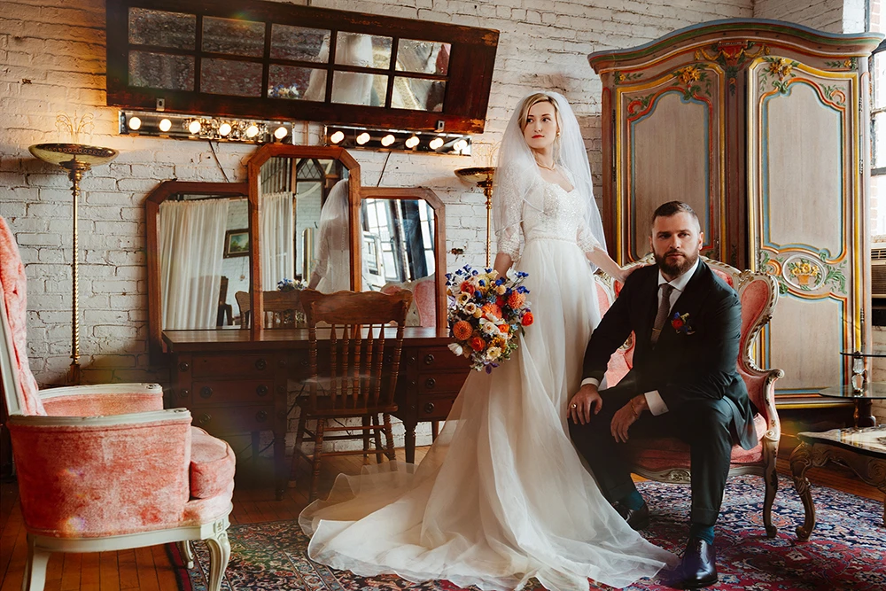 editorial style wedding image with couple surrounded with antique furniture in a soft light and bright colors